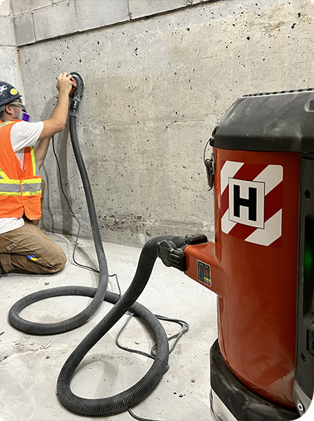 Meulage de béton sur mur intérieur avec aspirateur lors de la préparation de surface